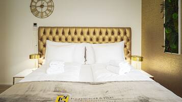 A neatly made bed with a tufted headboard, two bedside lamps, and a clock on the wall.