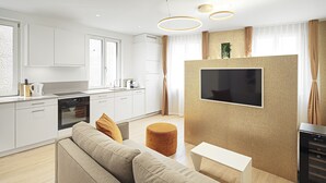 Una cocina moderna con armarios blancos, horno integrado y un comedor con mesa blanca y sofá beige.