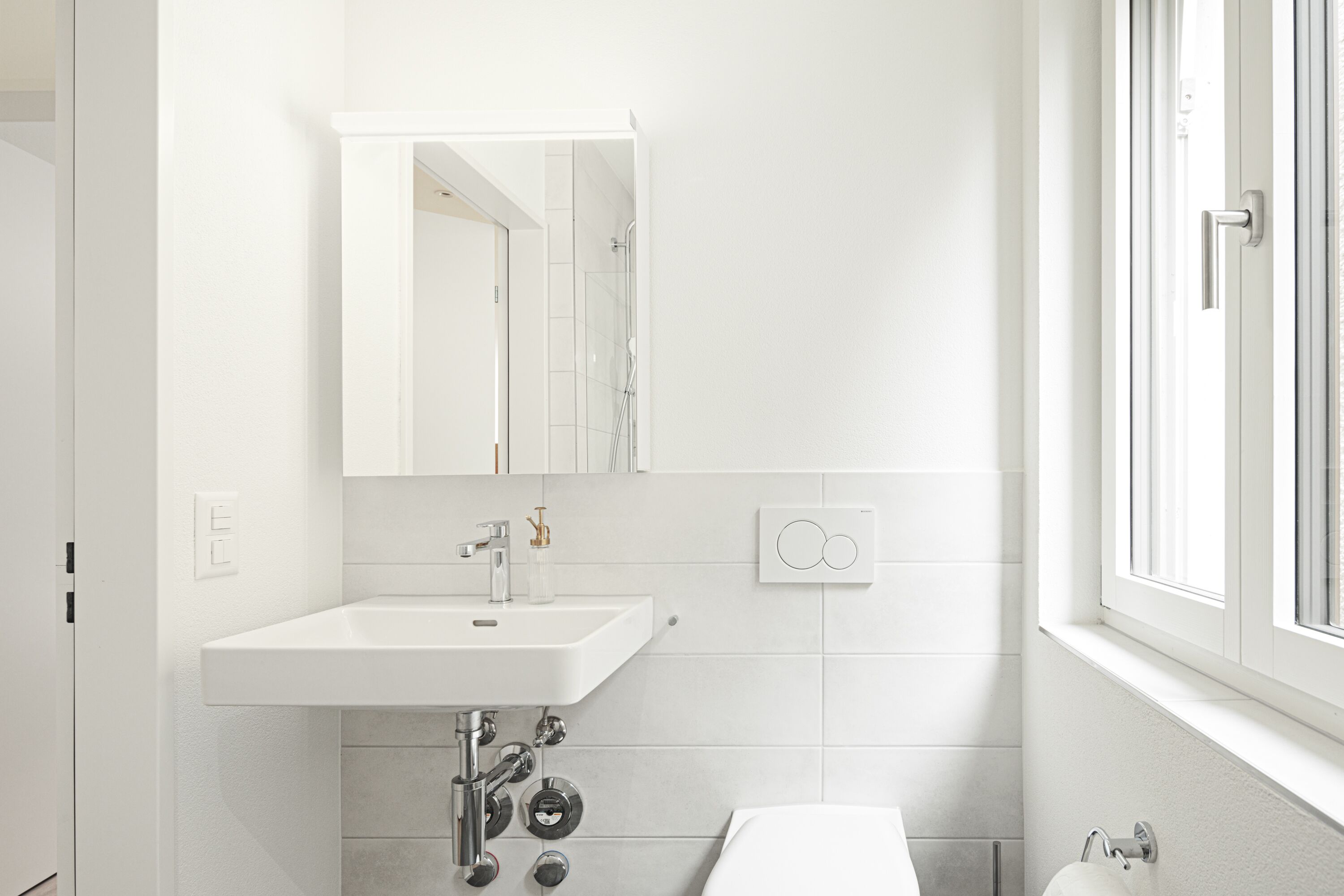 A modern bathroom with a white sink, mirror, and toilet.