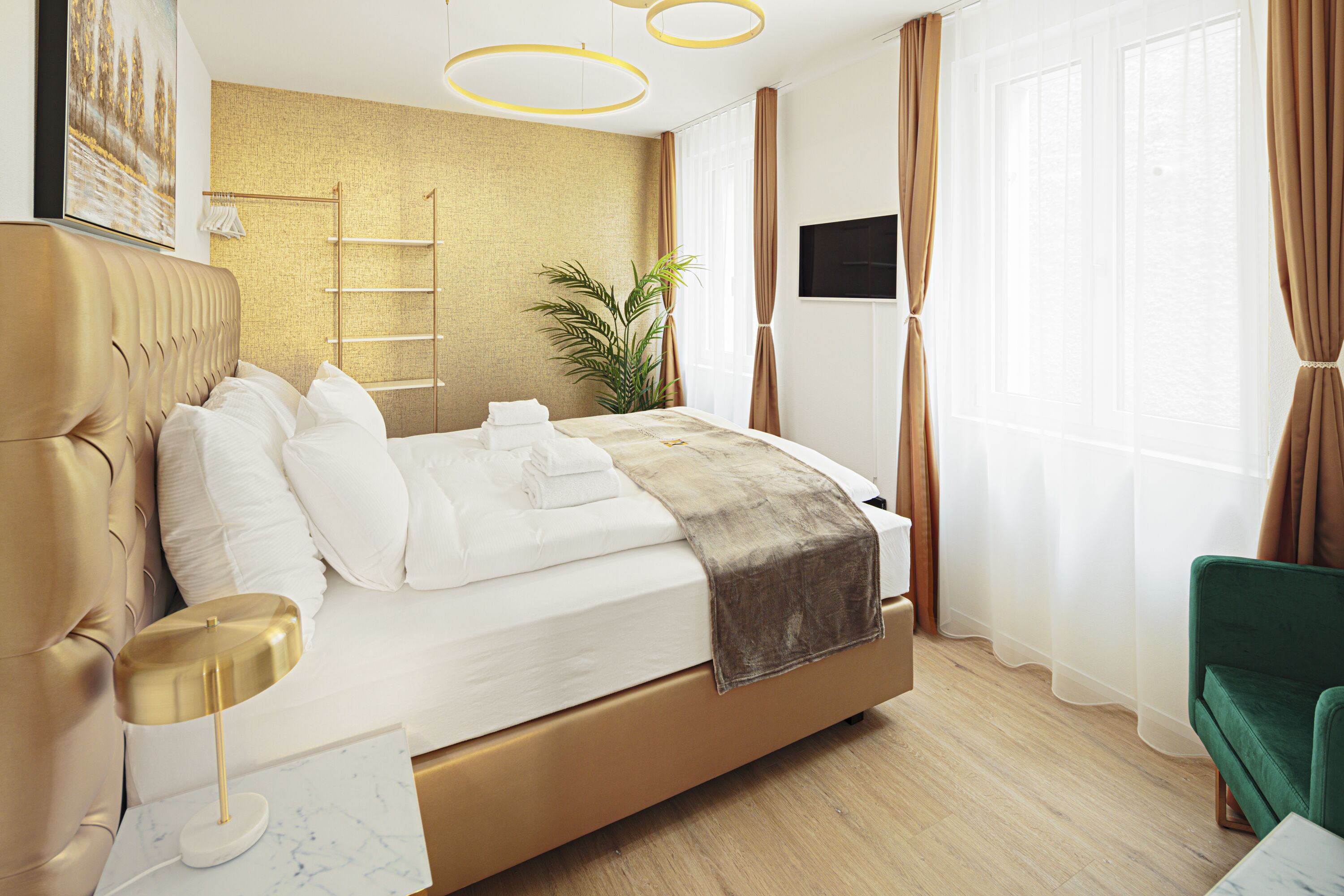 Una habitación de hotel moderna con una cama grande, una mesita de noche, un sillón verde, una planta y un televisor.