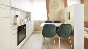 Una cocina moderna con armarios blancos, horno empotrado y comedor con mesa blanca y sillas verdes.