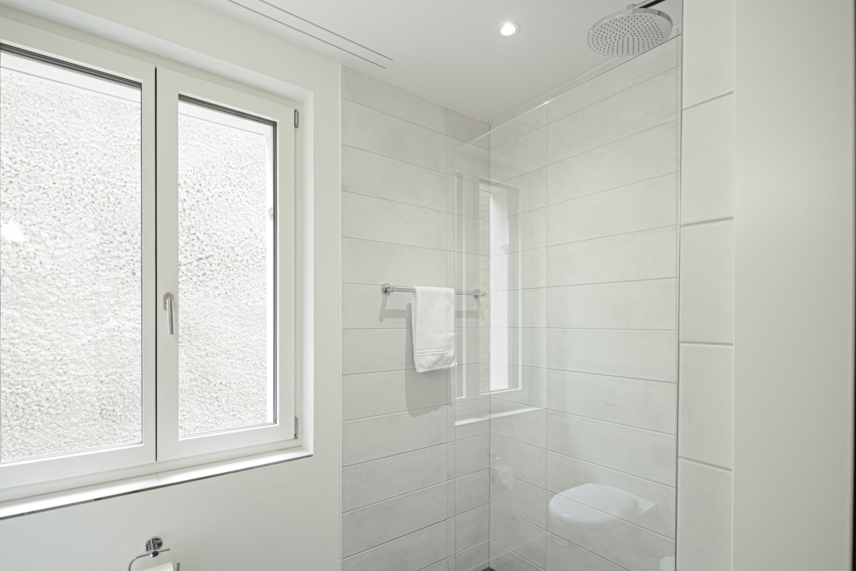 A modern bathroom with a large window, a glass shower enclosure, and a toilet.