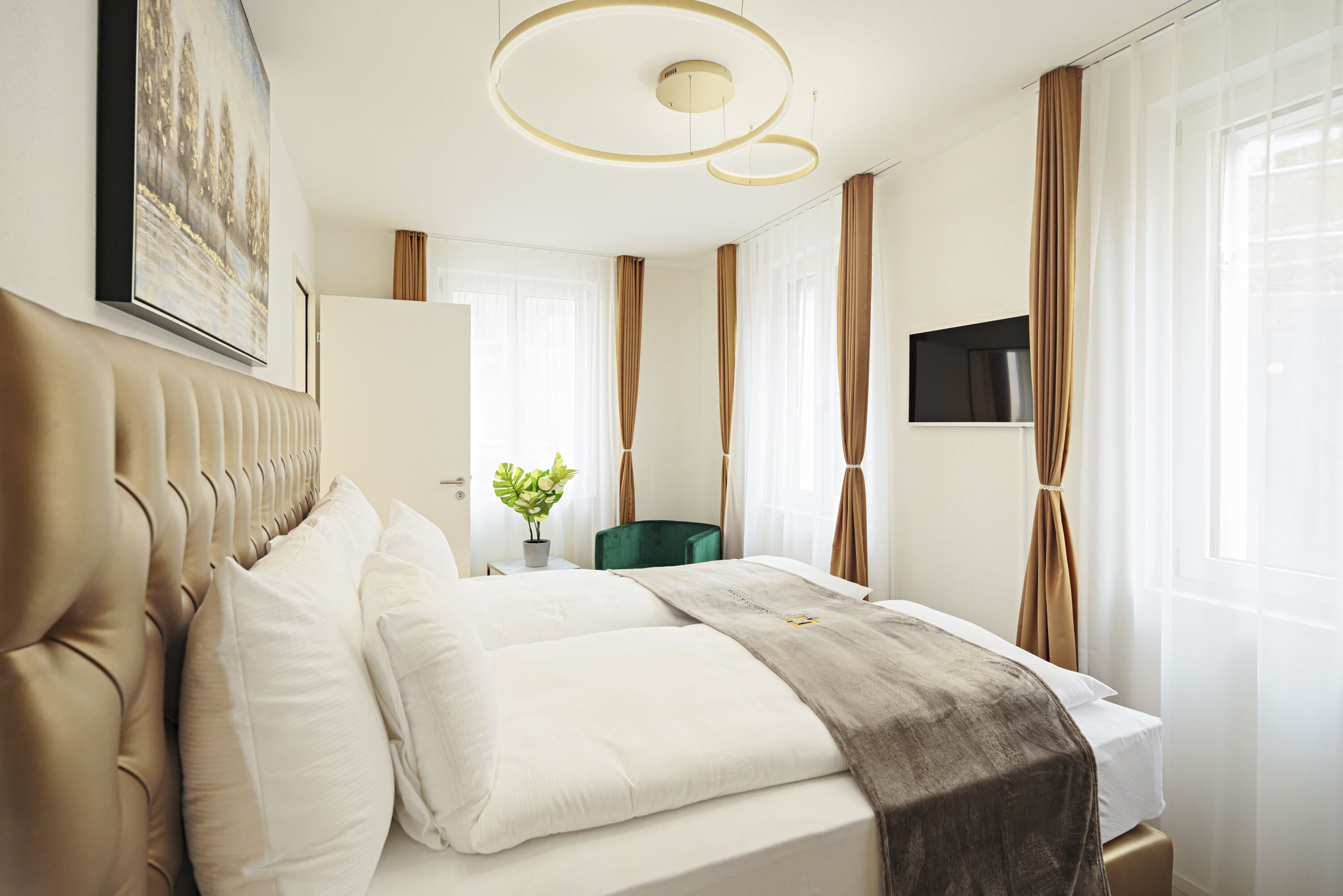 A modern hotel room with a large bed, a flat-screen TV, a desk with a chair, and a potted plant.