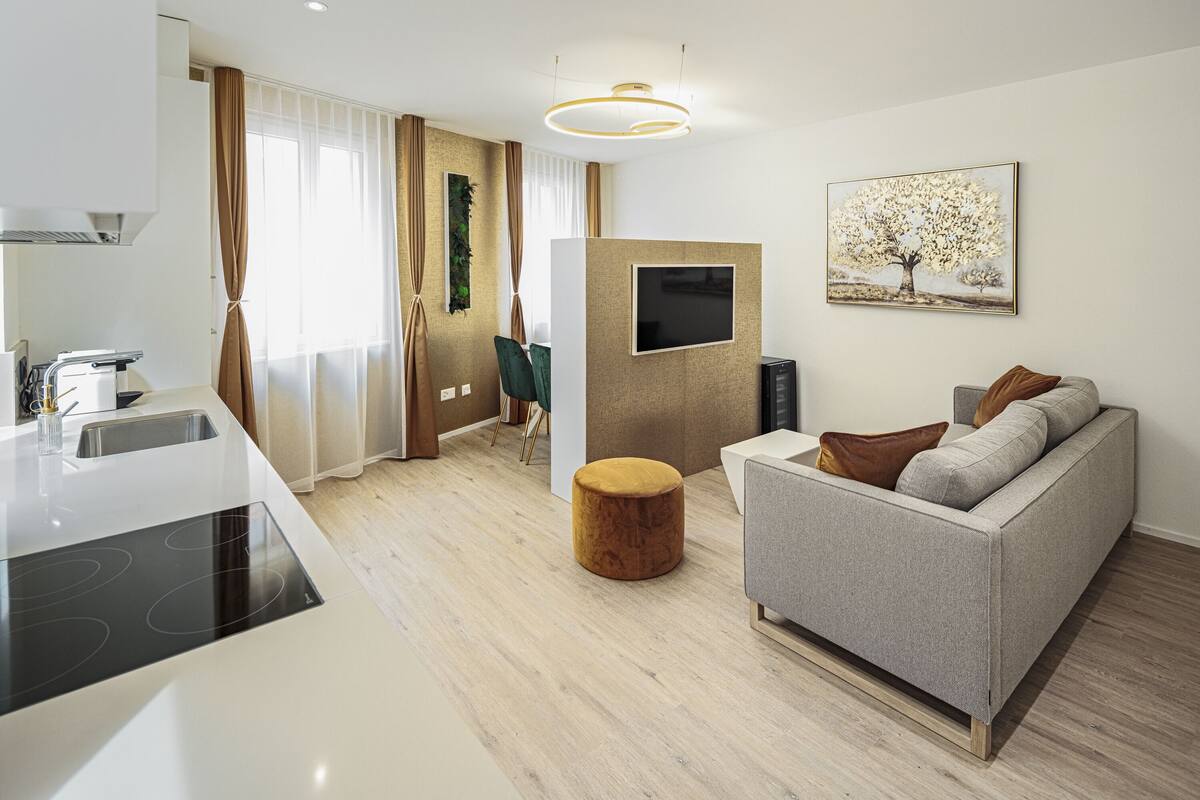 A modern living room with a sofa, a round wooden stool, a flat-screen TV, and a painting of a tree.