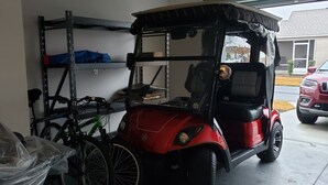 Un garaje con un carrito de golf rojo, una bicicleta y un estante metálico.