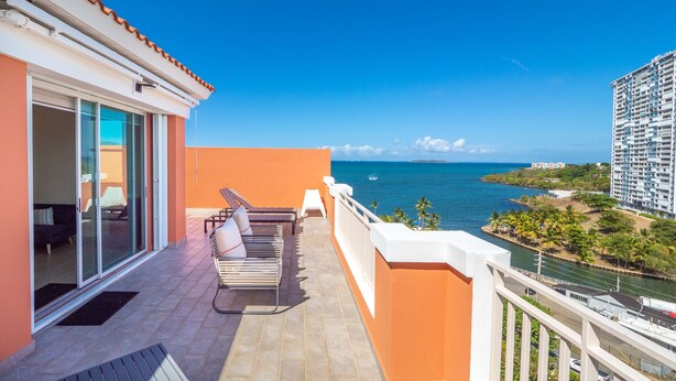 Ein Balkon mit Meerblick, ein Poolbereich mit Liegestühlen und ein Gebäude mit roter Fassade.