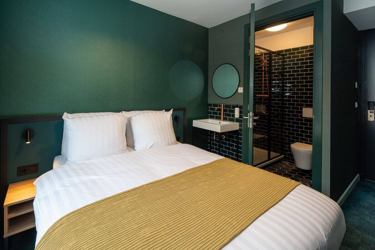 A hotel room with a bed, a bedside table, a bathroom with a sink and toilet, and a mirror.