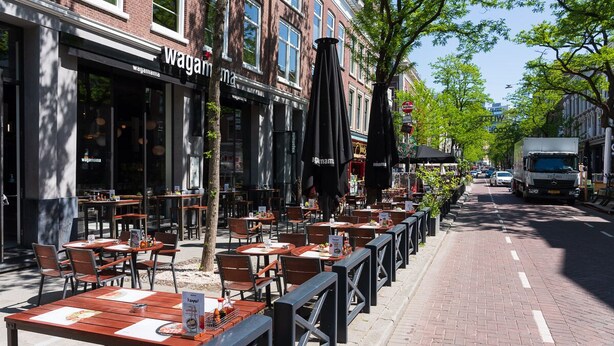 An outdoor cafe with tables and chairs, a brick building with 'Wagamama' signage, and a truck parked on the street.