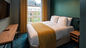 A hotel room with a large bed, a desk, and a window with curtains.