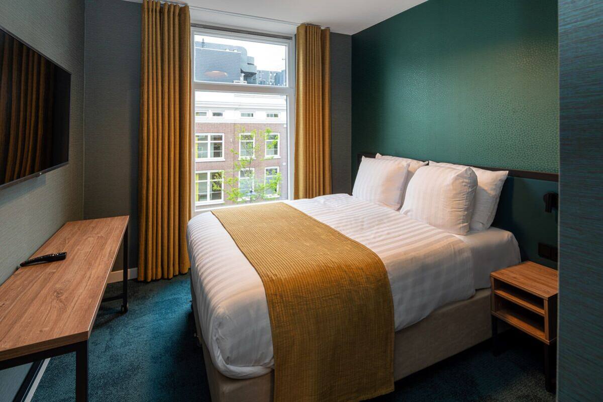 A hotel room with a large bed, a desk, and a window with curtains.