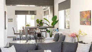 Ein modernes Wohnzimmer mit einer Couch, einem Essbereich mit Stühlen, einem Tisch und einer großen Pflanze.