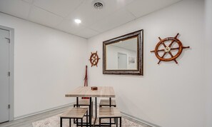 Una habitación con una mesa de madera y cuatro sillas, un espejo grande y dos adornos de timón de barco en la pared.