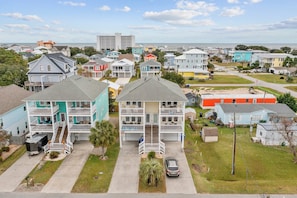 A residential area with multi-story houses, a visible street, and a clear view of the ocean.
