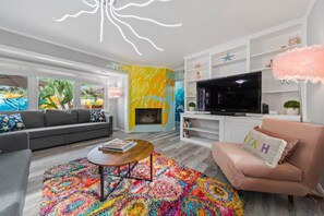 A modern living room with a sofa, a pink armchair, a coffee table, a TV, and a colorful rug.