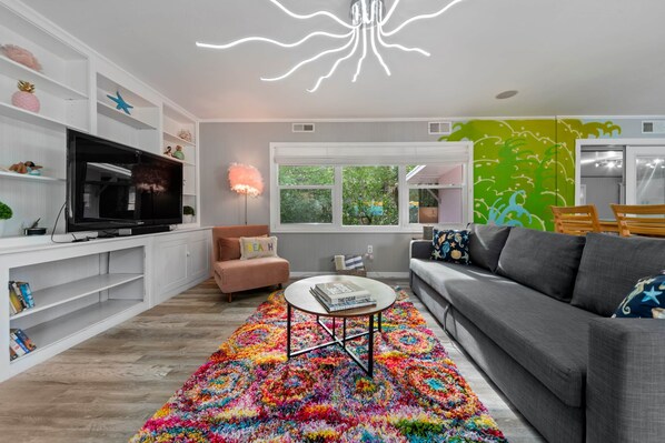 A modern living room with a flat-screen TV, a colorful rug, a gray sofa, and a white coffee table.