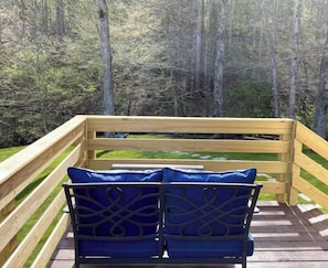 A wooden deck with a bench and a railing, overlooking a forested area.