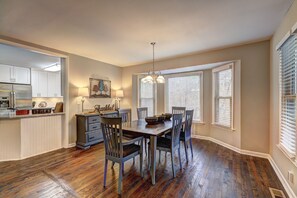 A dining area with a wooden table and chairs, a chandelier, and a view of the kitchen.