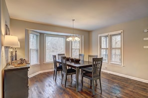 A dining area with a wooden table, six chairs, a chandelier, and a sideboard with a lamp and decorative items.