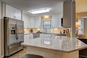 A modern kitchen with white cabinetry, a stainless steel refrigerator, granite countertops, and a built-in stove.