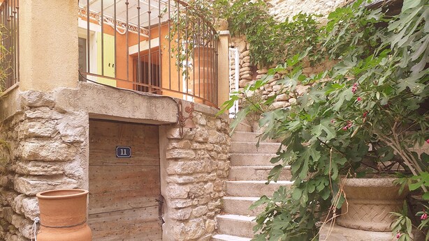 A stone staircase leading to a wooden door with a number plate, surrounded by greenery and a terracotta pot.