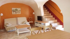 A cozy living room with a sofa, a coffee table, and a TV stand. There is a staircase with a red railing leading to an upper level.