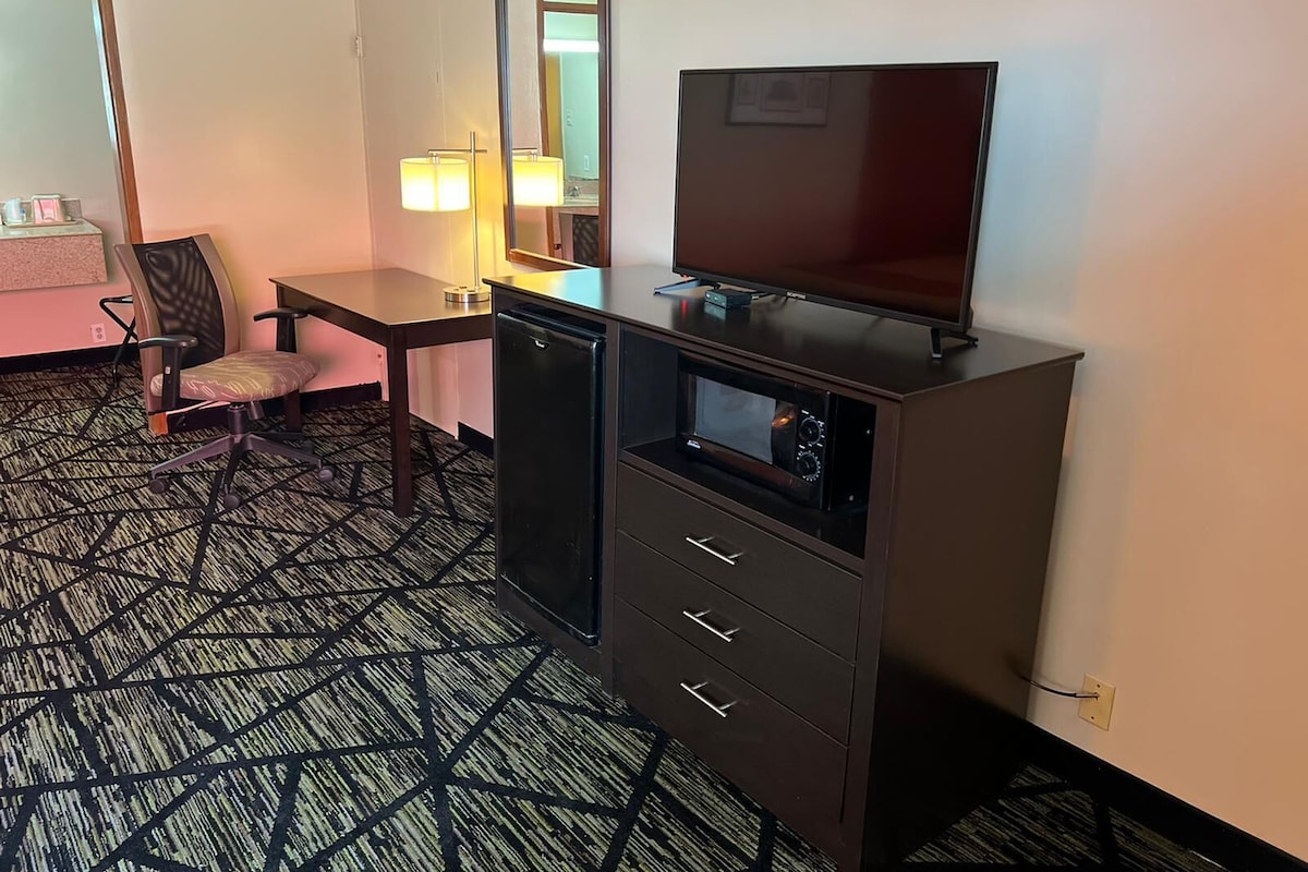 A hotel room with a desk, chair, television, and a minibar.