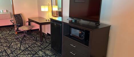 A hotel room with a desk, chair, television, and a minibar.