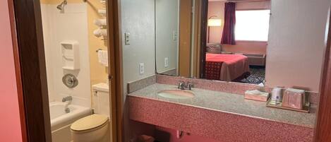 A hotel bathroom with a shower, toilet, sink, and a large mirror.