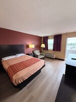 Una habitación de hotel con cama, escritorio, silla, lámpara y ventana con cortinas.