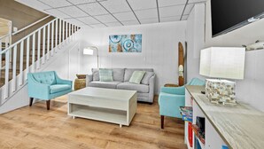Ein Wohnzimmer mit Treppe, einem grauen Sofa, einem weißen Couchtisch und einem an der Wand befestigten Fernseher.