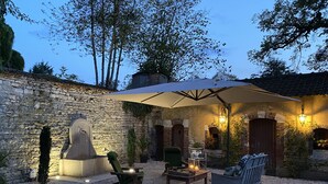 An outdoor patio area with stone walls, a stone fireplace, and outdoor furniture under a large umbrella. - Manoir De La Croix Saint Louis (Les Hauts de Forterre)