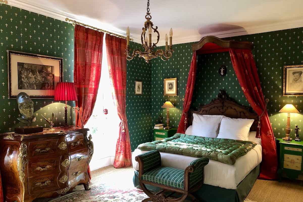 A bedroom with a four-poster bed, green patterned wallpaper, and a chandelier.