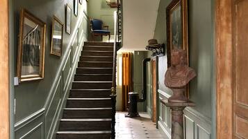 Un grand escalier orné d’une rampe, menant à un palier où se trouvent un buste sculpté et des œuvres d’art encadrées.