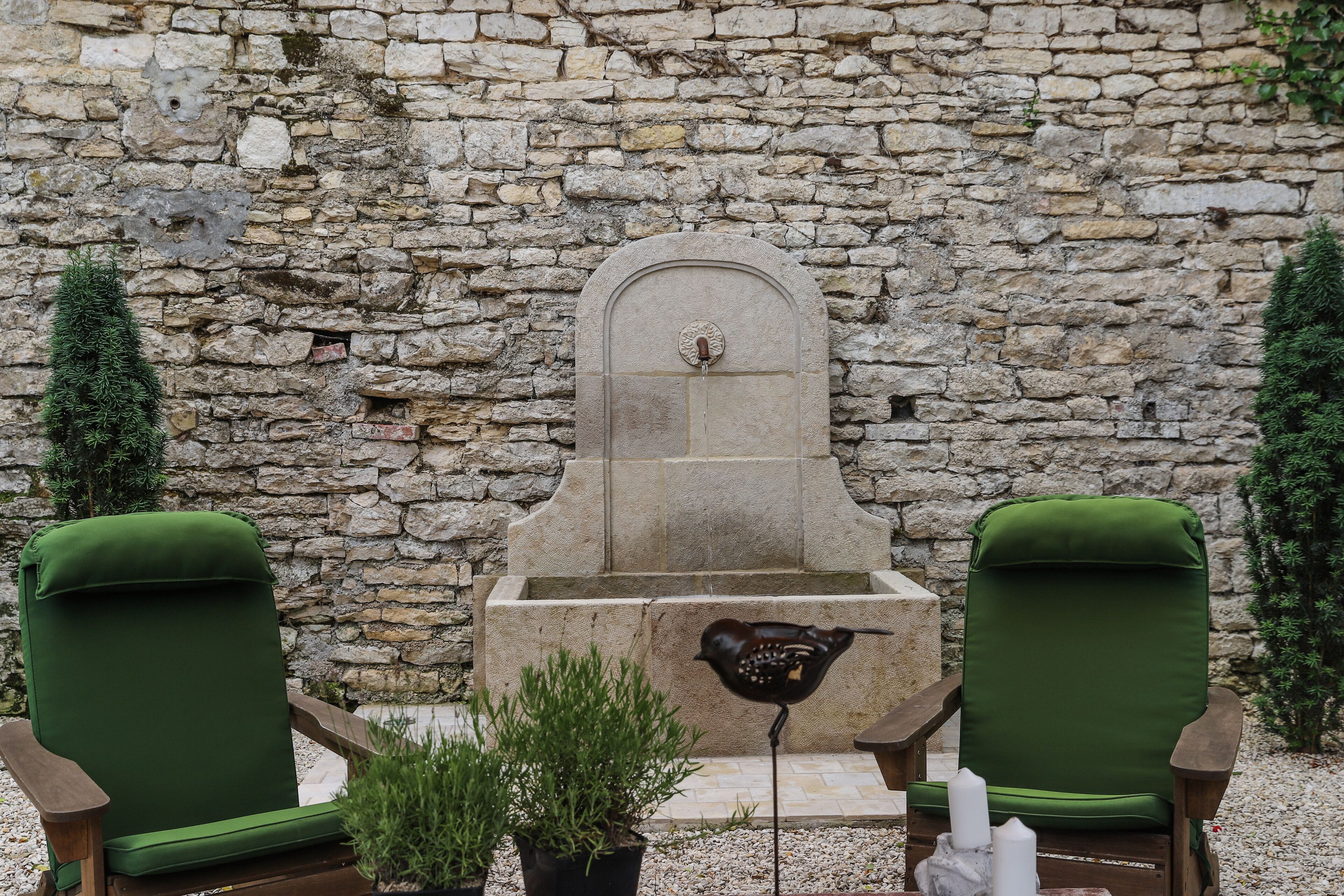 Two green upholstered chairs facing a stone wall with a fountain.