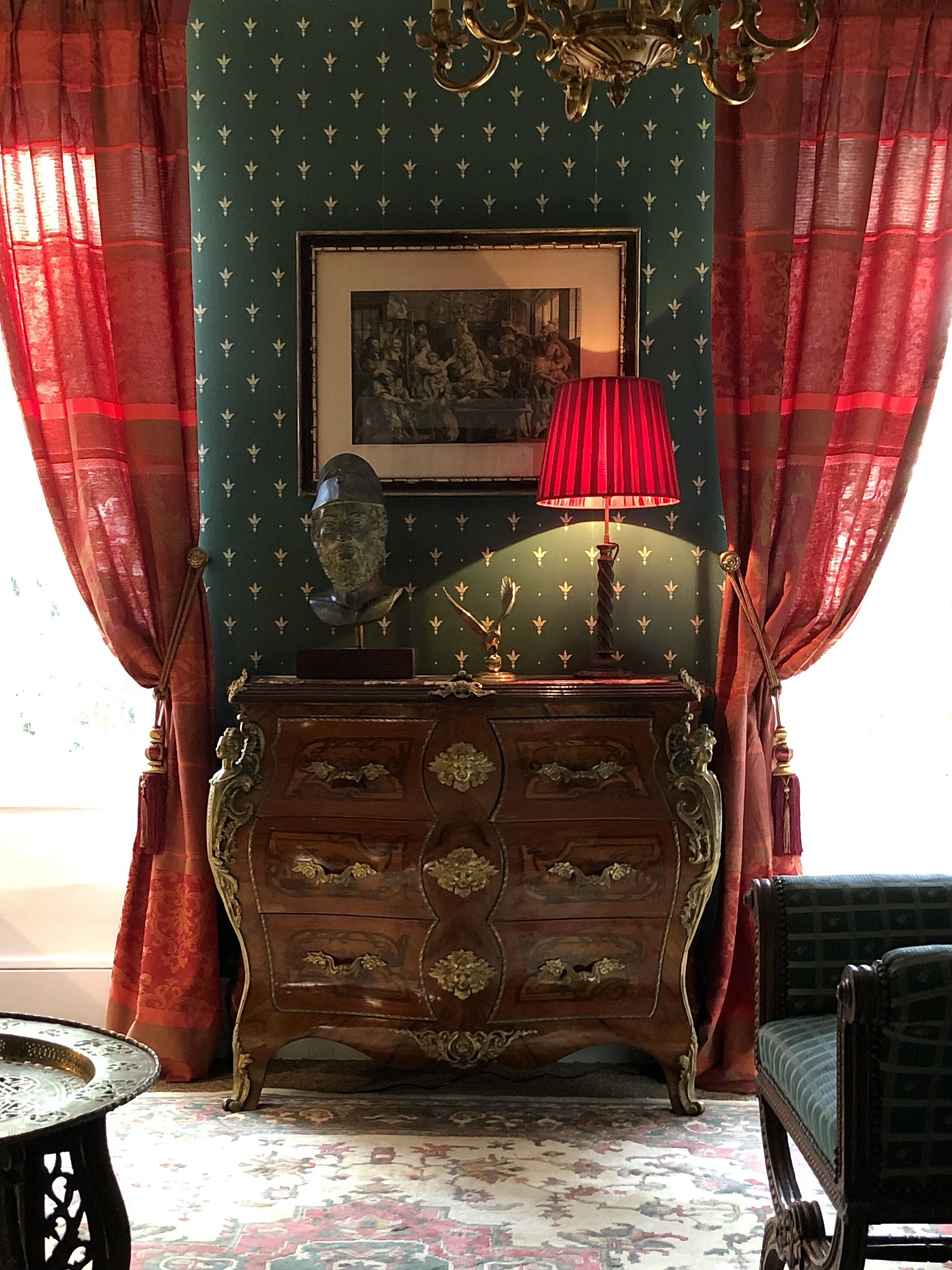 A room with a green wall, a framed painting, a red lamp, a wooden cabinet, and a patterned carpet.