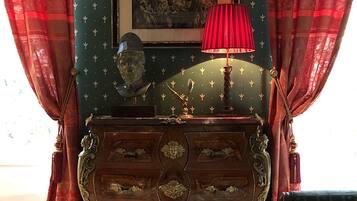 A room with a green wall, a framed painting, a red lamp, a wooden cabinet, and a patterned carpet.