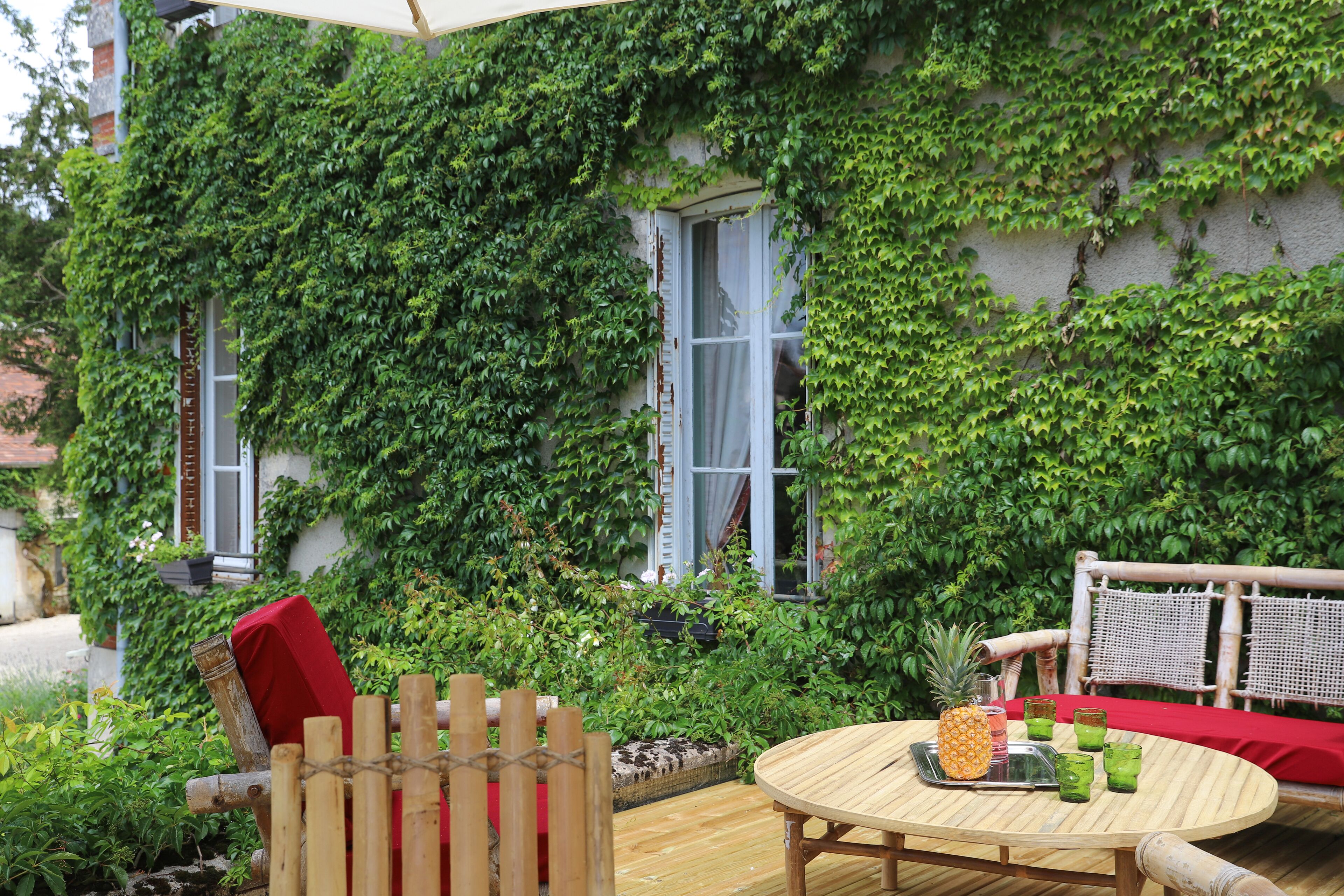 An outdoor patio with a wooden table, a red cushion, and a wicker chair.