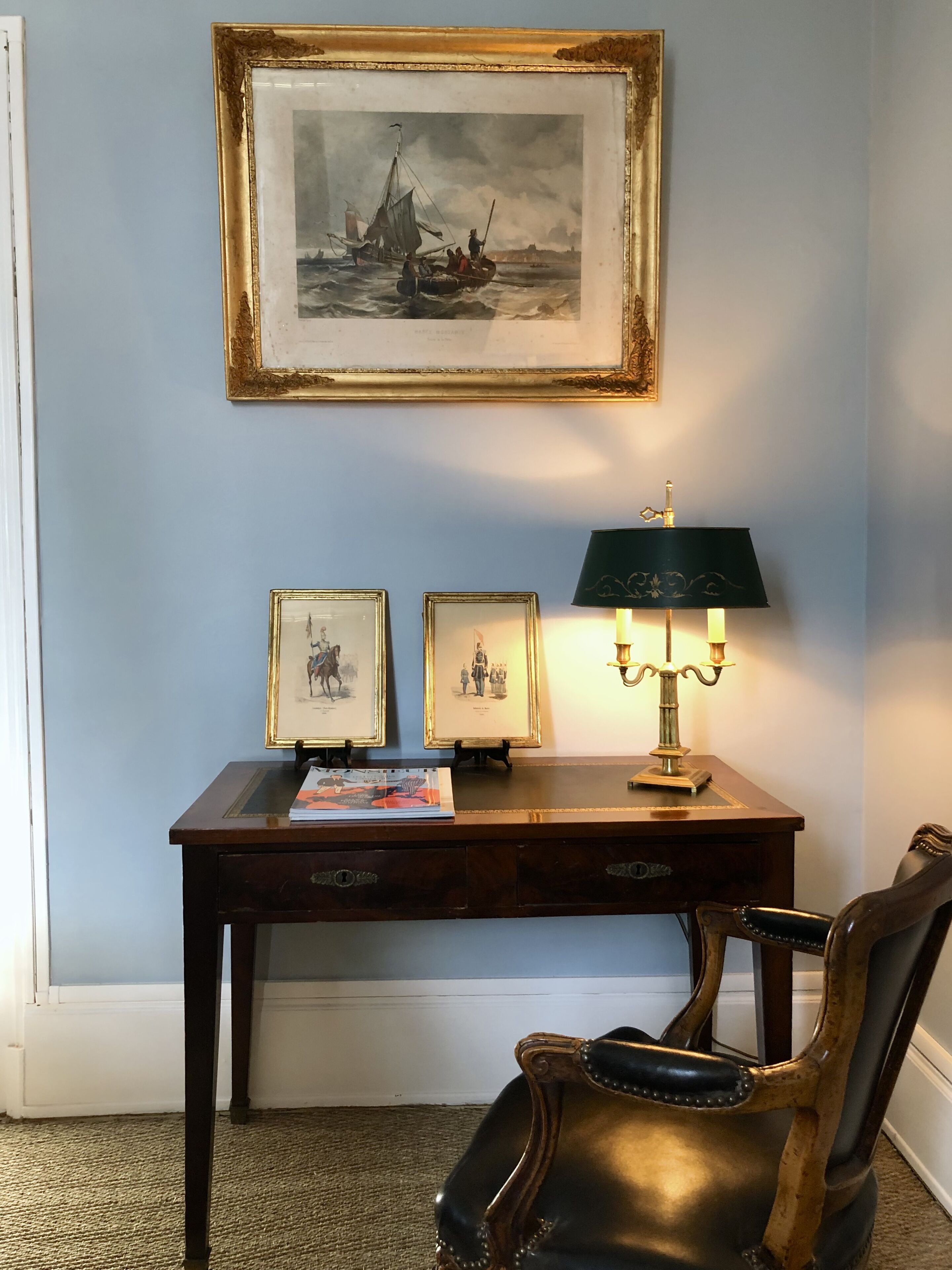 A room with a desk, framed artwork, a lamp, and a leather chair.