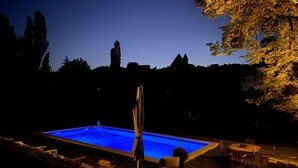 A swimming pool with a covered umbrella, surrounded by outdoor furniture and a patio area. - Manoir De La Croix Saint Louis (Les Hauts de Forterre)