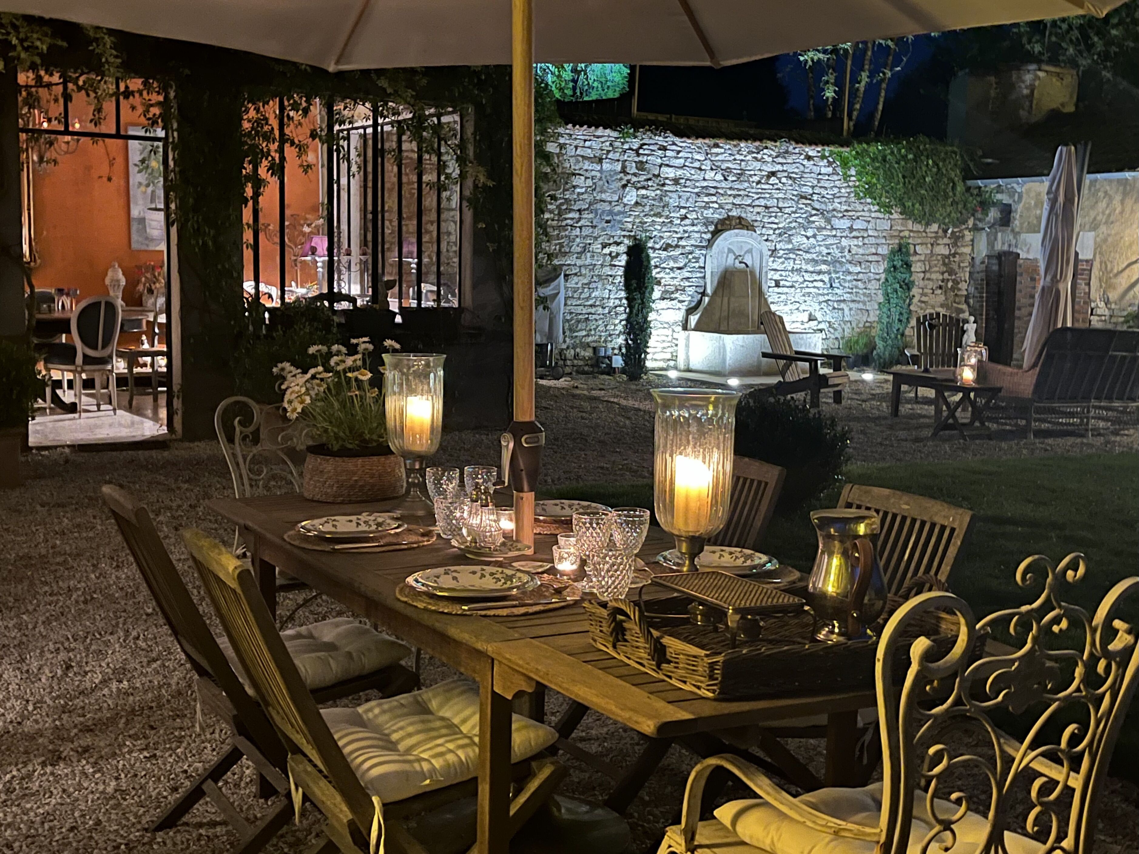 An outdoor dining area with a stone wall backdrop, a wooden table set for two, and a rustic outdoor seating arrangement.