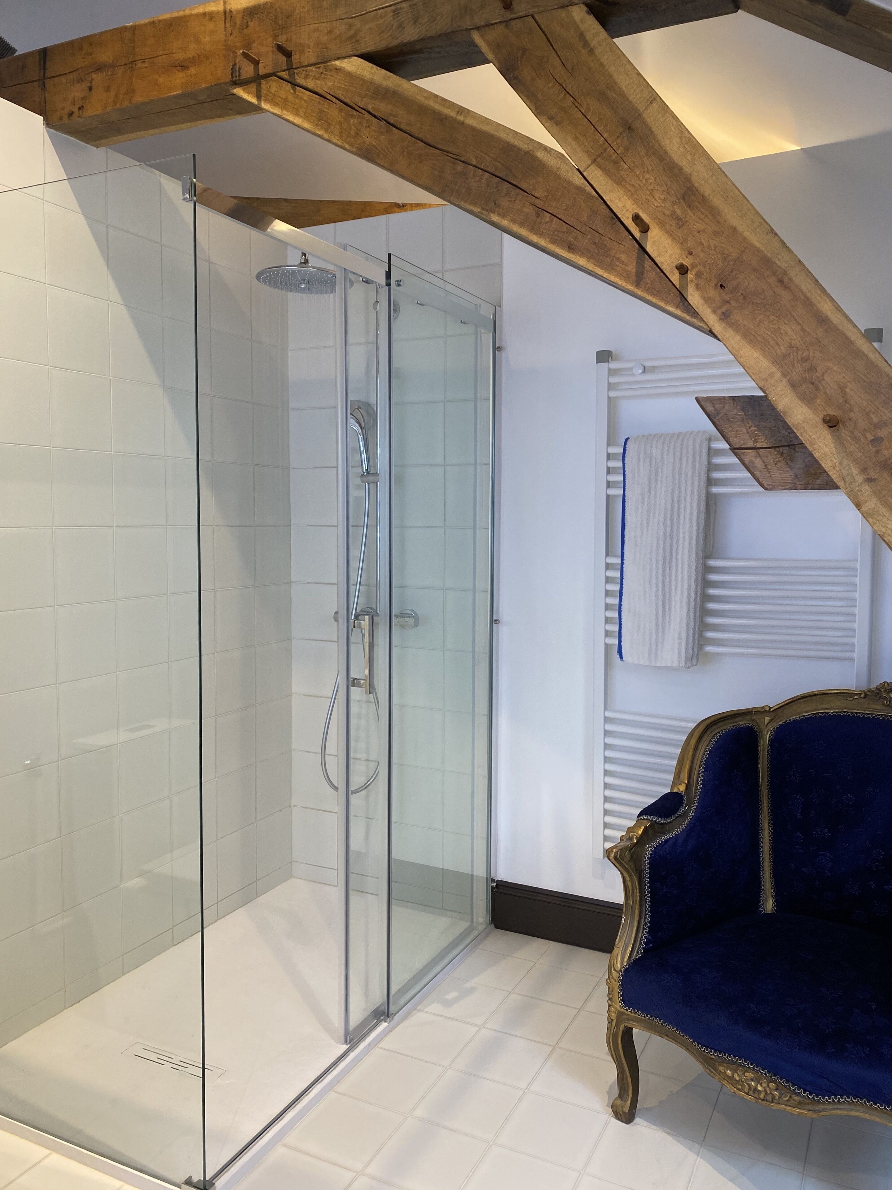 Une salle de bain moderne avec une douche à parois de verre, des murs recouverts de carreaux blancs et une poutre en bois au plafond.
