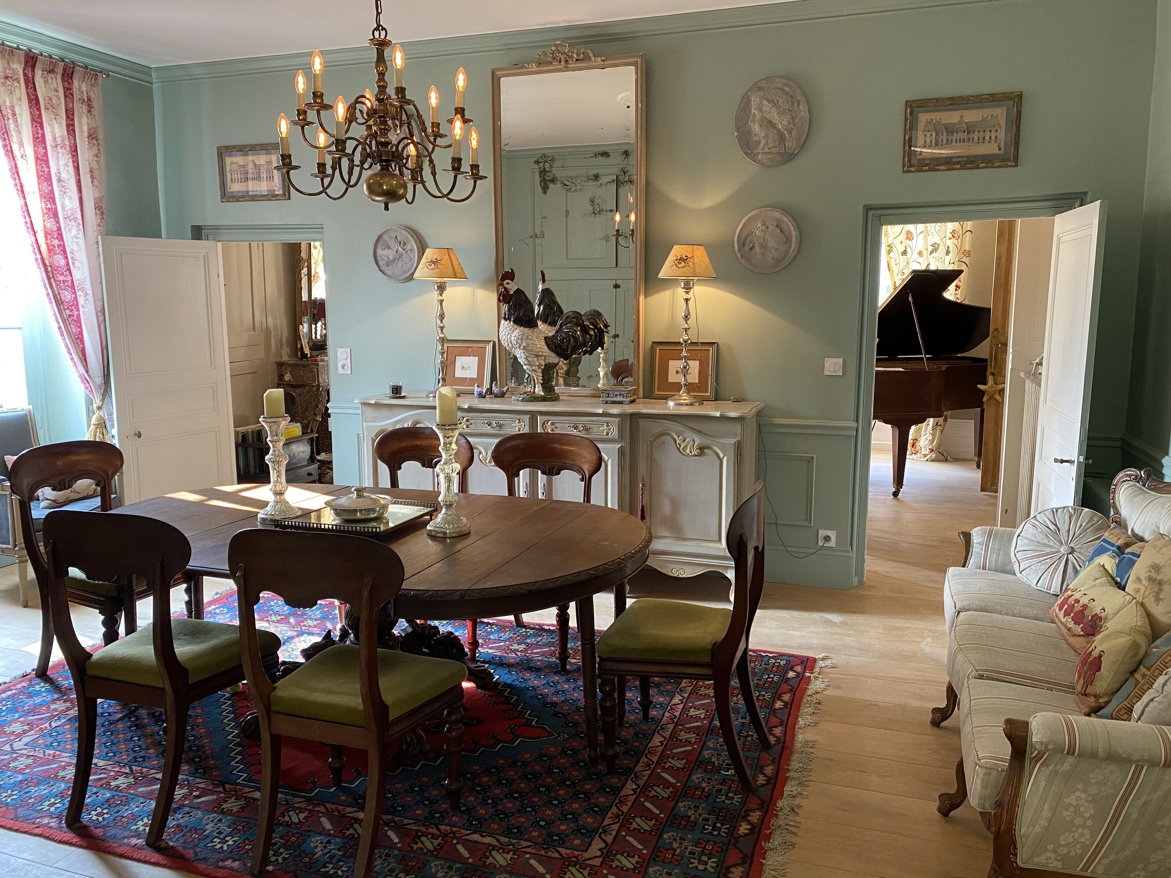 A dining area with a round table, chairs, a chandelier, and a patterned rug.