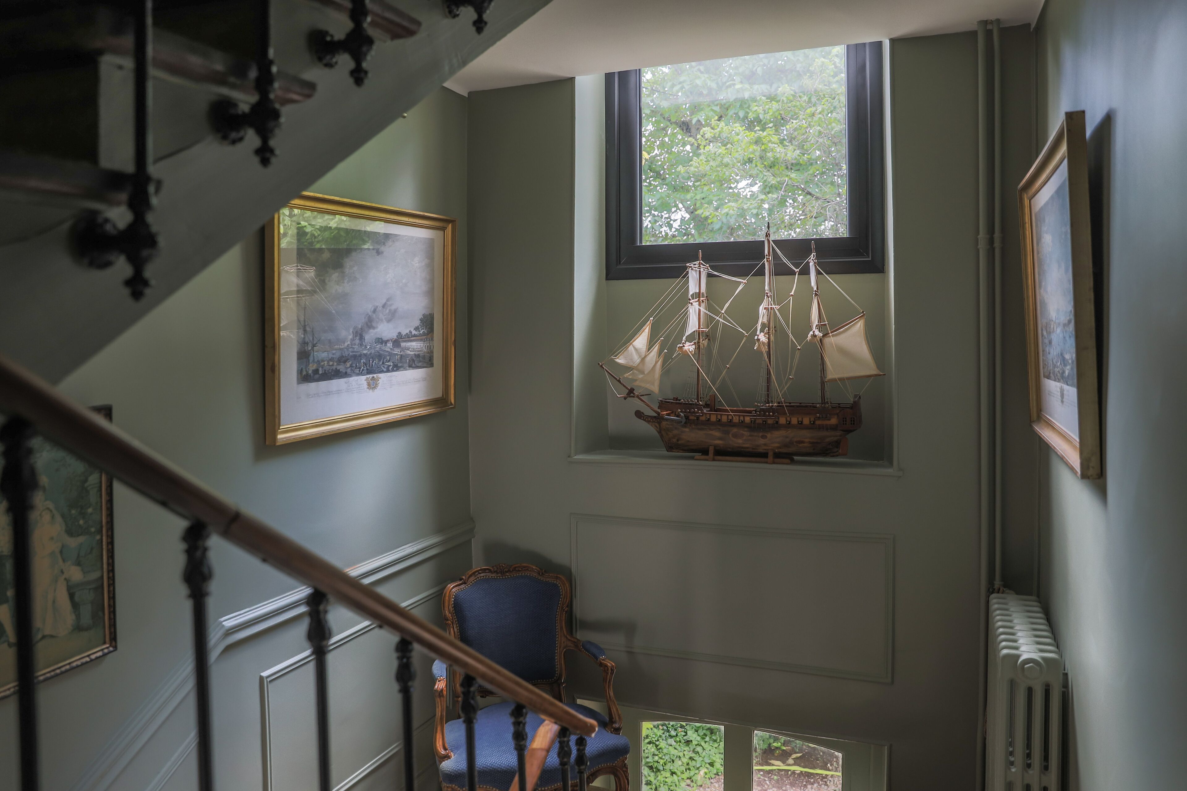 A staircase with a chair and a ship model on the wall.