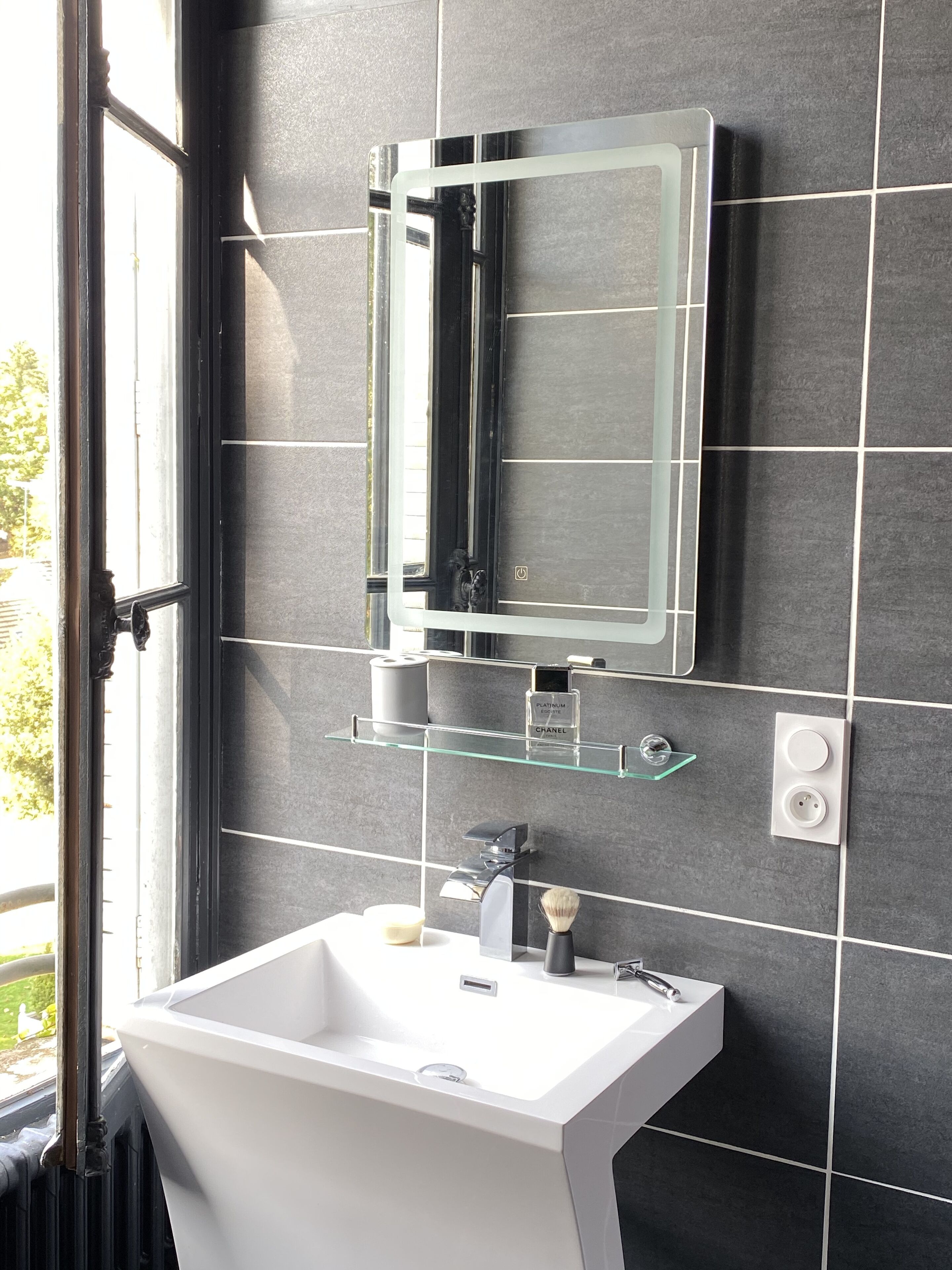A modern bathroom with a white sink, a glass shelf with toiletries, and a mirror above it.