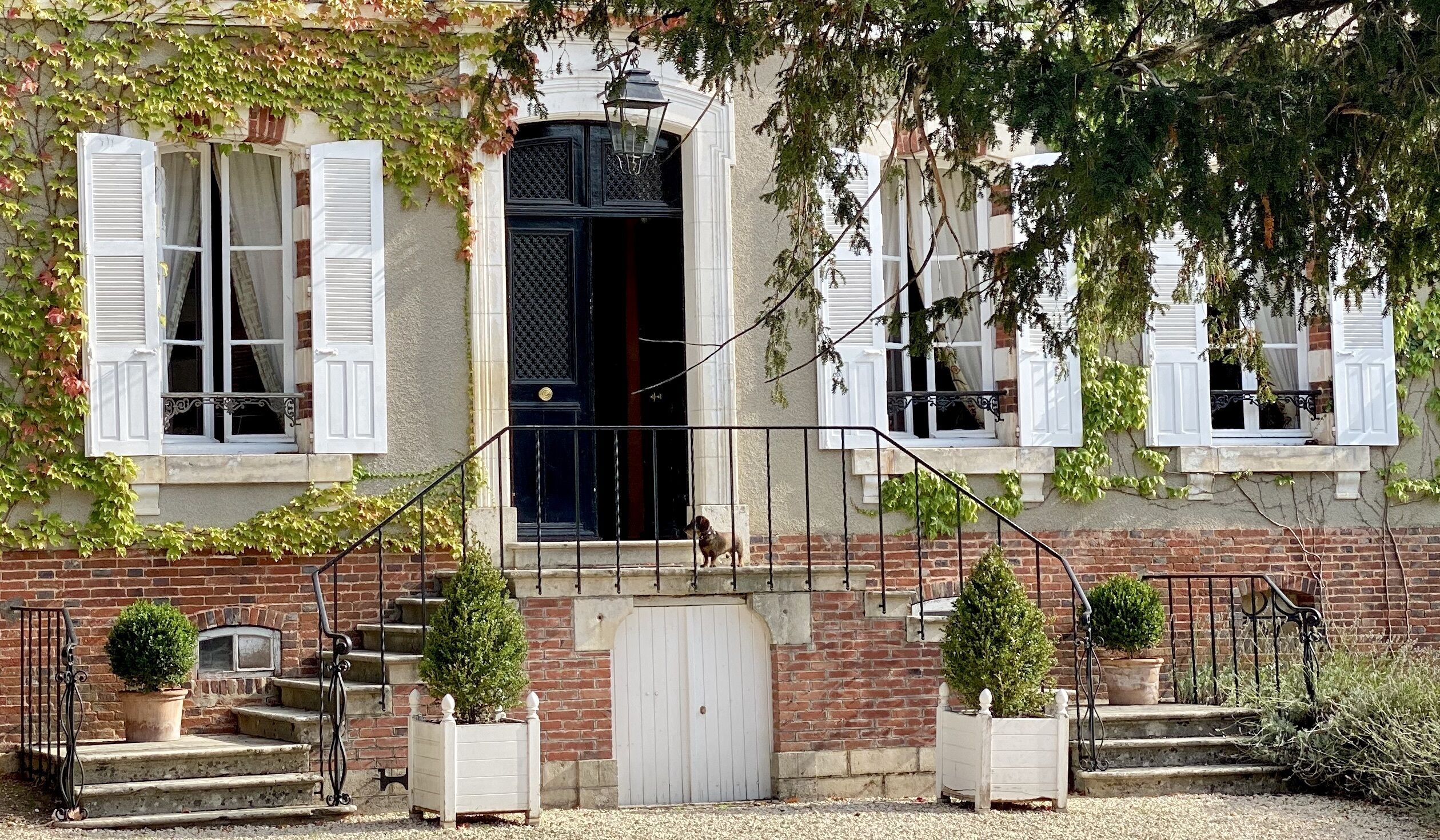 Il s’agit d’un bâtiment traditionnel avec une façade en briques, des volets blancs et une porte noire. Des marches mènent à une porte blanche et un petit balcon agrémenté d’une balustrade.