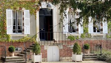 Il s’agit d’un bâtiment traditionnel avec une façade en briques, des volets blancs et une porte noire. Des marches mènent à une porte blanche et un petit balcon agrémenté d’une balustrade.