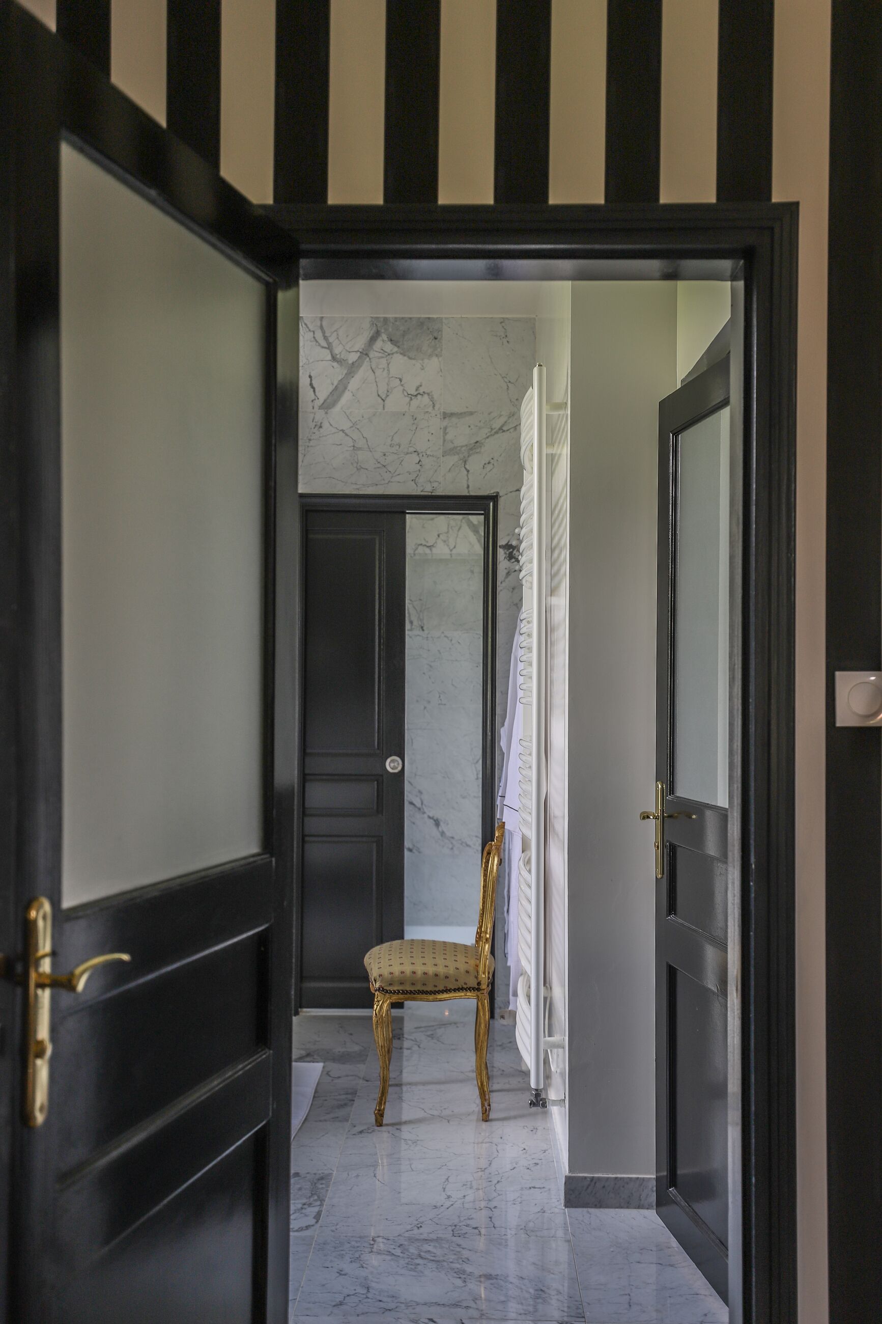 A hallway with a marble floor, a chair, and a door with a black and white striped pattern.