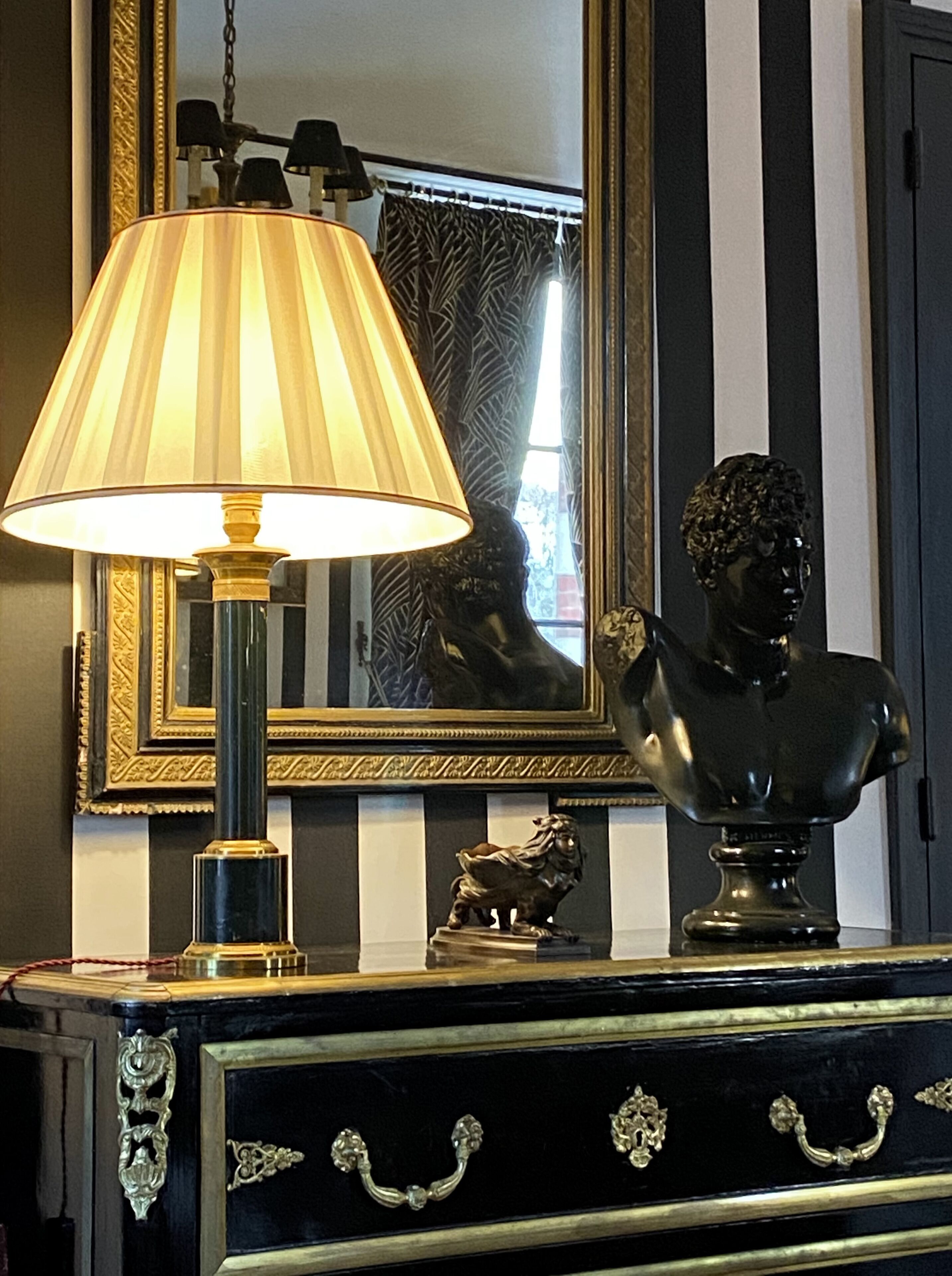 Un aparador negro y dorado con ornamentación, una lámpara, un busto de escultura y un espejo con marco decorativo.