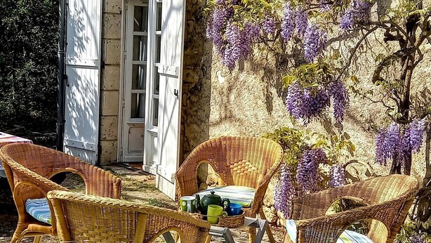 Un bâtiment rustique en pierre doté d’un patio couvert, aménagé avec des meubles en osier et une table.
