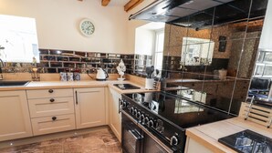 Una cocina con suelo de baldosas de piedra, una estufa negra y un reloj blanco en la pared.